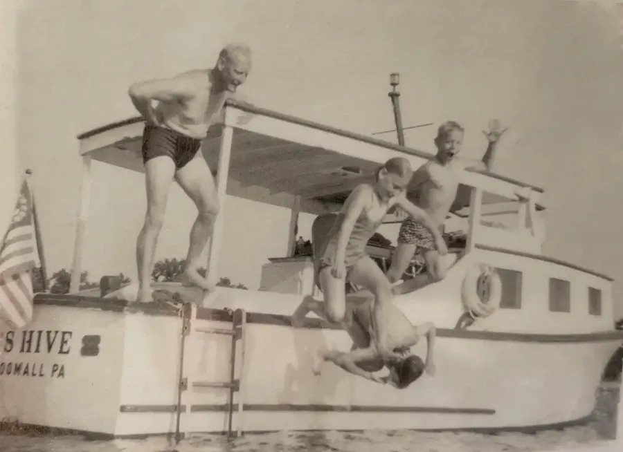 Black-and-white photo from June 1963: Bruce as a boy (far right, waving) with his family jumping off his dad's converted Chesapeake deadrise